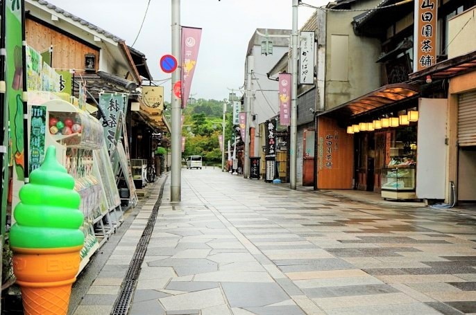 A tiled street lined with shops, gatcha machines, and a green tea soft serve ice cream display